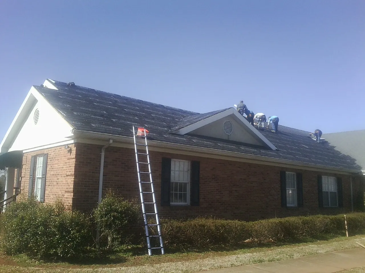 Crew tearing shingles off a brick ranch roof with a ladder set — Emergency Roof Repair work by our crew in Brookline